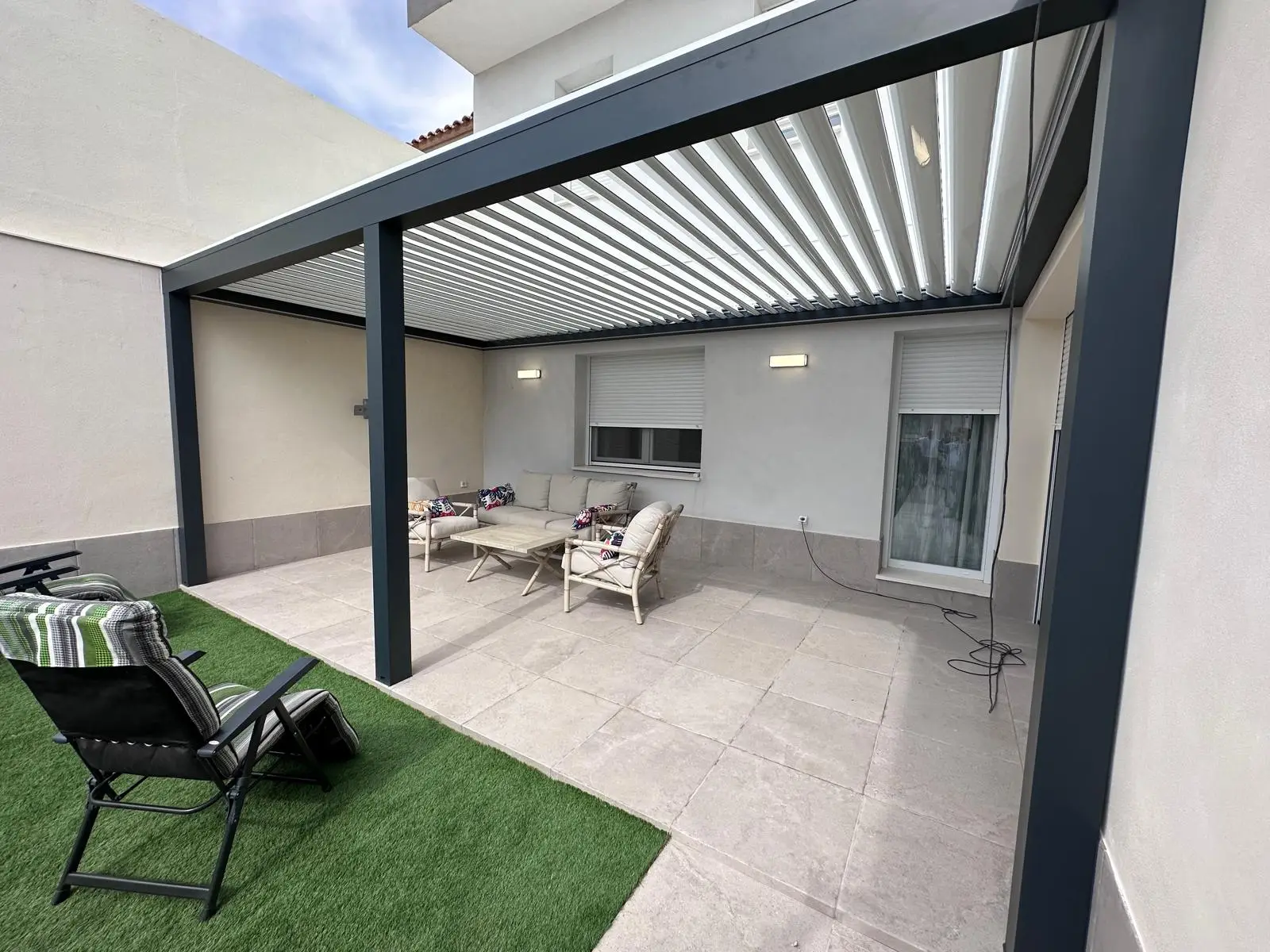 Pérgola bioclimática gris antracita con lamas orientables sobre una zona de estar